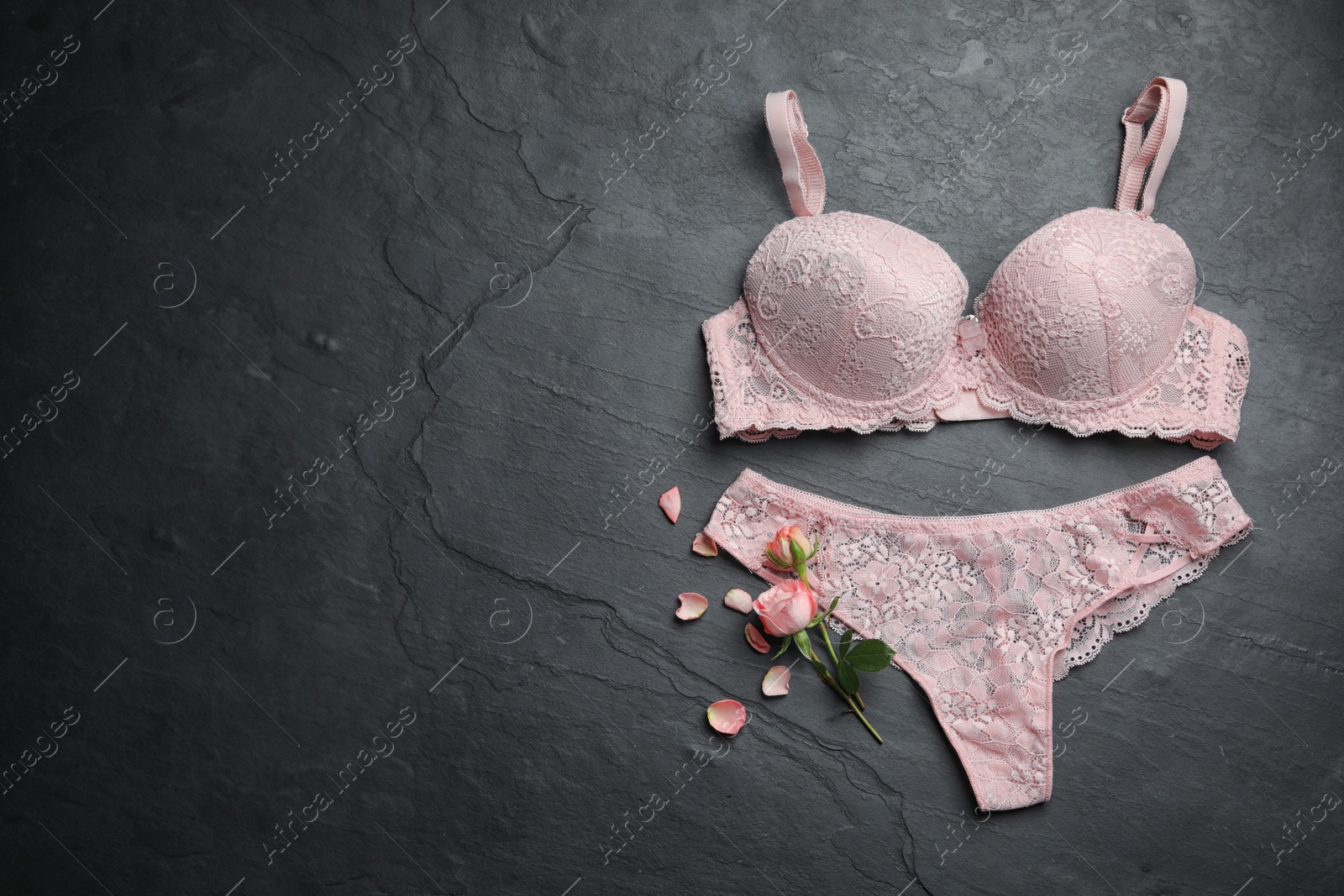 Photo of Elegant women's underwear and flowers on black stone background, flat lay. Space for text