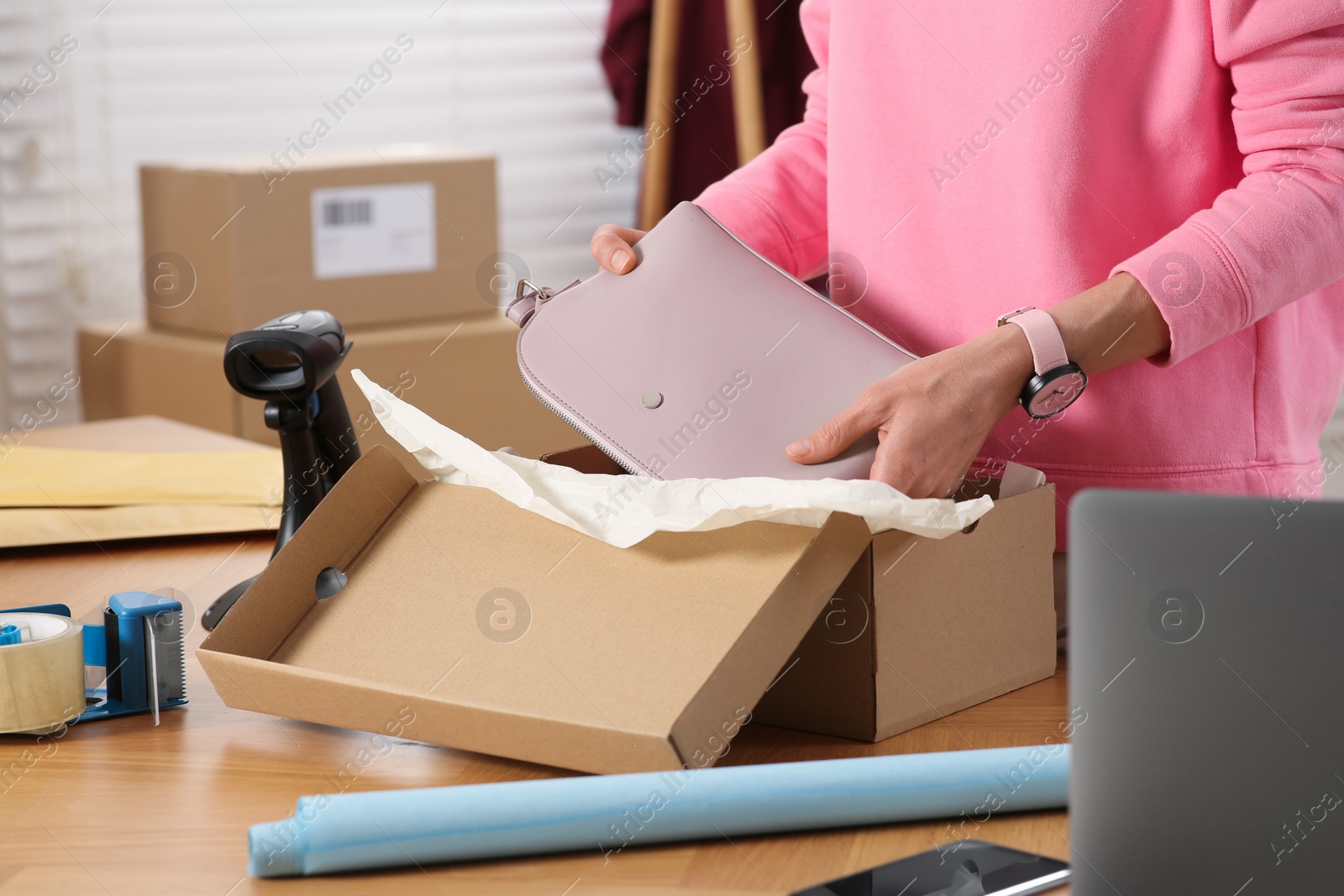 Photo of Seller packing bag into cardboard box at table in office, closeup. Online store