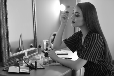 Portrait of beautiful woman applying makeup indoors, black and white effect