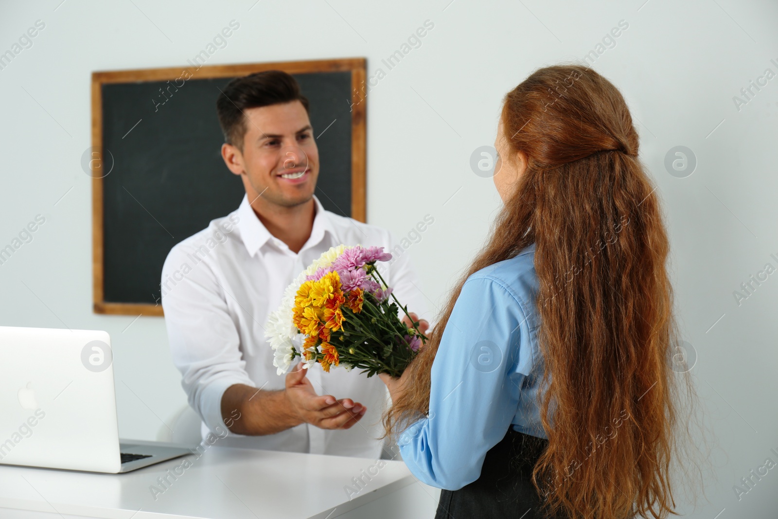 Photo of Schoolgirl congratulating her pedagogue with bouquet in classroom. Teacher's day