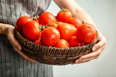 Photo of Woman holding wicker bowl with ripe tomatoes, closeup