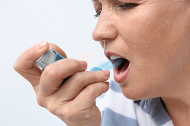Image of Woman using asthma inhaler on white background, closeup