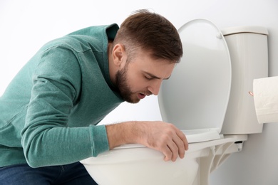 Photo of Young man suffering from nausea over toilet bowl indoors