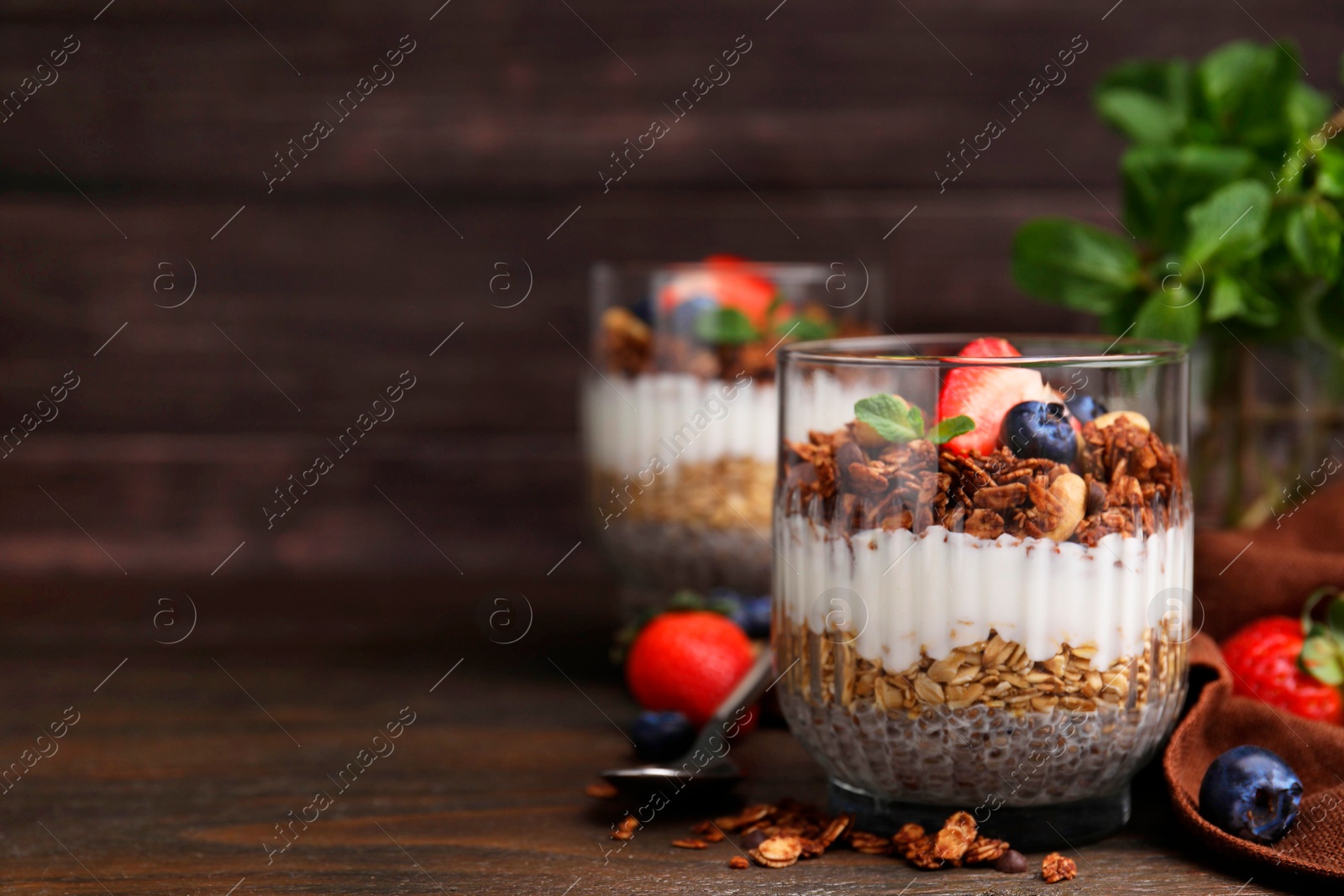 Photo of Tasty granola with berries, nuts, yogurt and chia seeds on wooden table, space for text