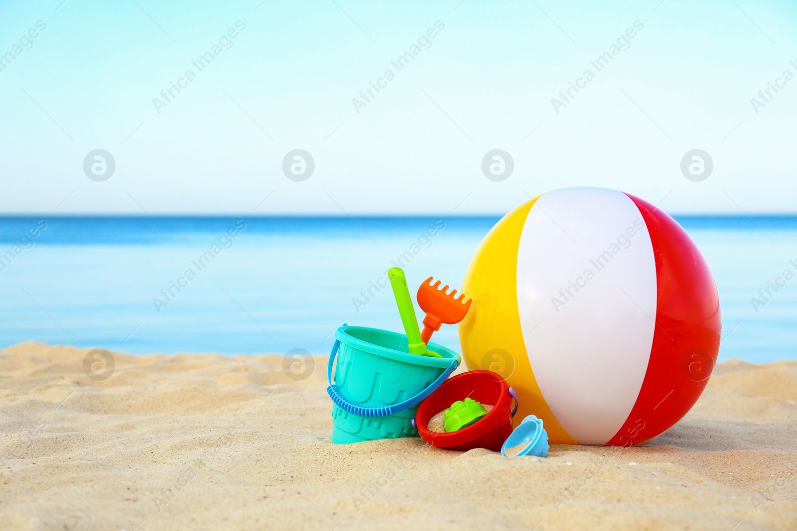 Photo of Set of plastic beach toys and colorful ball on sand near sea. Space for text