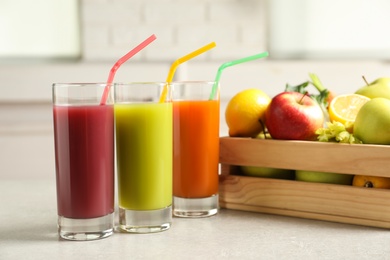 Photo of Three glasses of juices next to wooden crate with fresh ingredients on light table