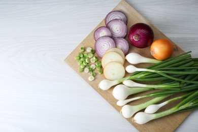 Photo of Board with different kinds of onions on white wooden table, top view. Space for text