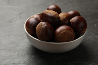 Photo of Roasted edible sweet chestnuts in bowl on grey textured table, closeup