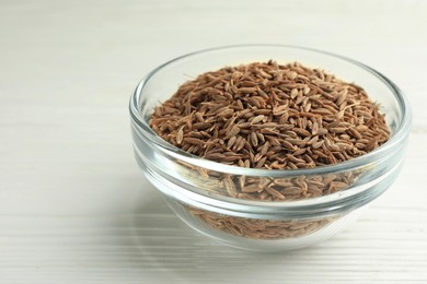 Bowl of caraway seeds on white wooden table, closeup