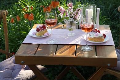 Photo of Vase with spring flowers, wine and cake on table served for romantic date in garden