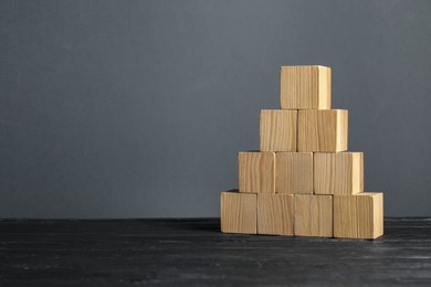 Photo of Pyramid of blank cubes on dark wooden table. Space for text