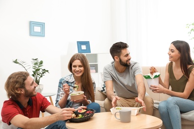 Photo of Young people having lunch together in living room. Food delivery
