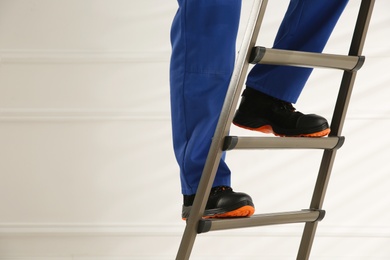 Photo of Professional worker climbing up ladder indoors, closeup view