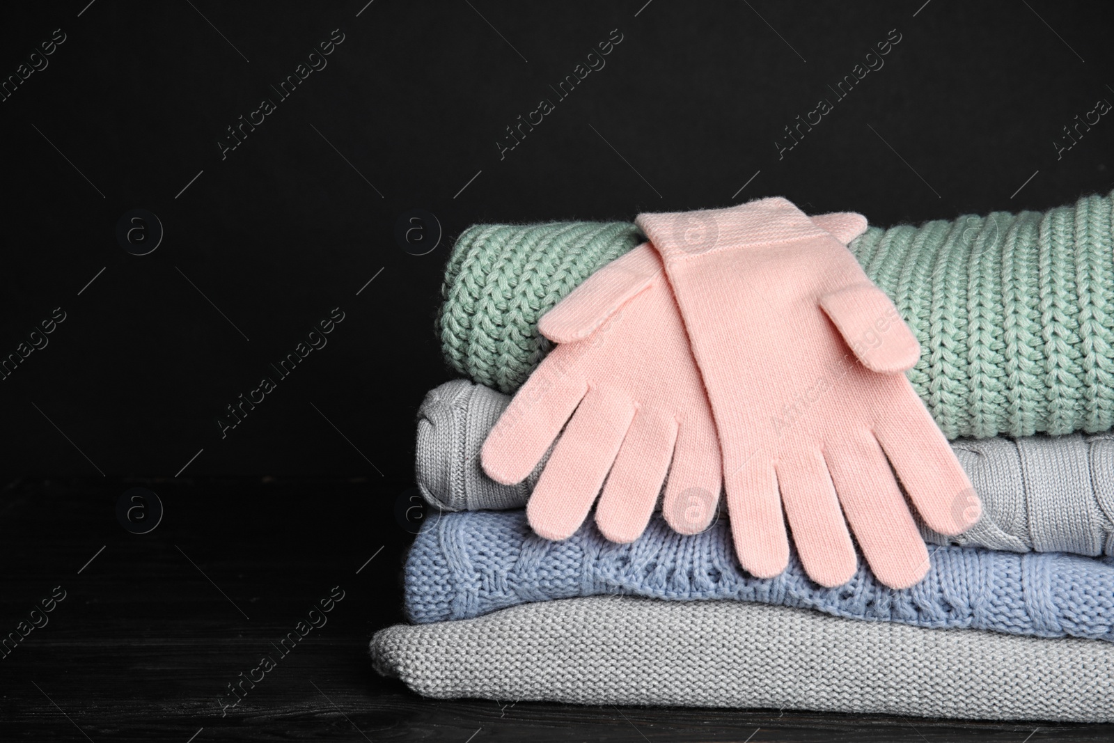 Photo of Stacked sweaters and gloves on table, closeup with space for text. Autumn clothes