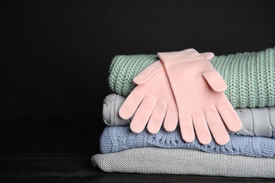 Photo of Stacked sweaters and gloves on table, closeup with space for text. Autumn clothes