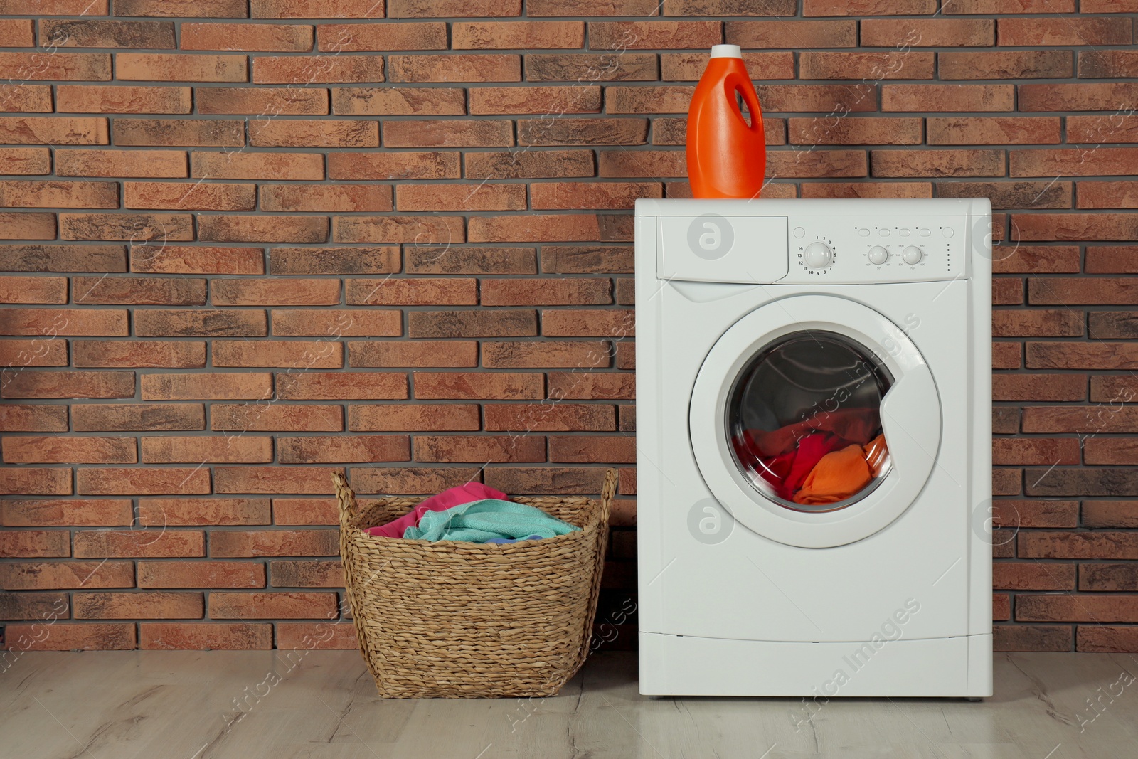 Photo of Modern washing machine with laundry, detergent and wicker basket near brick wall. Space for text
