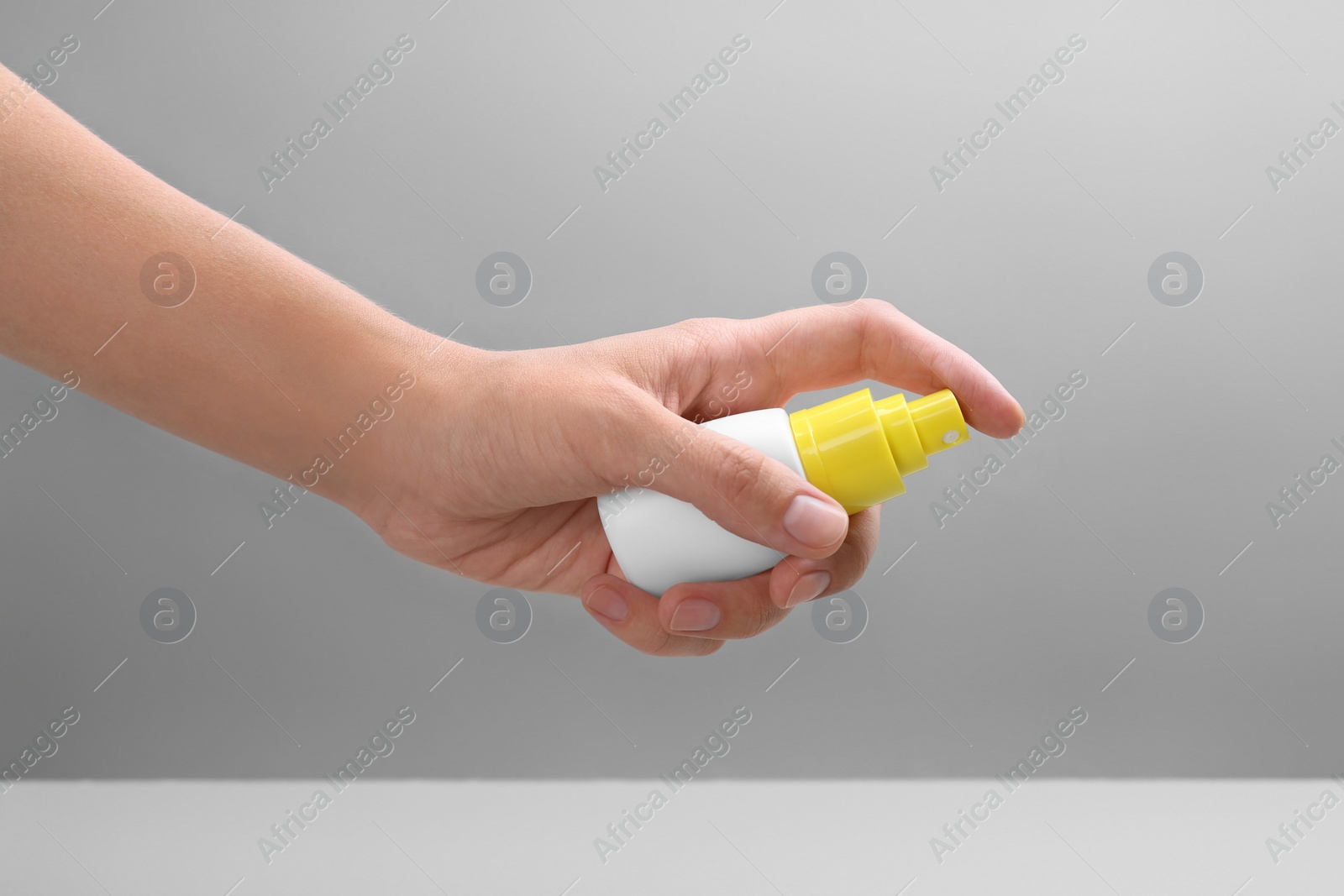 Photo of Woman with bottle of insect repellent spray on grey background, closeup