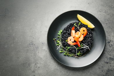 Delicious black risotto with shrimps and lemon on grey table, top view. Space for text
