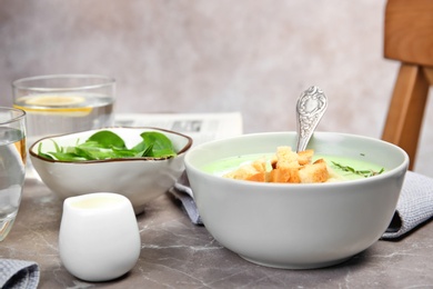 Photo of Green pea soup with croutons in bowl on table