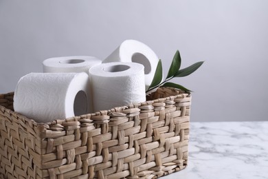 Photo of Toilet paper rolls and green leaves in wicker basket on white marble table, space for text