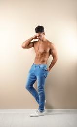 Shirtless young man in stylish jeans near light wall