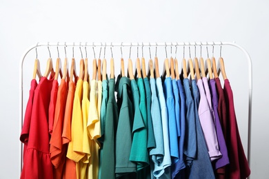 Rack with bright clothes on light background. Rainbow colors