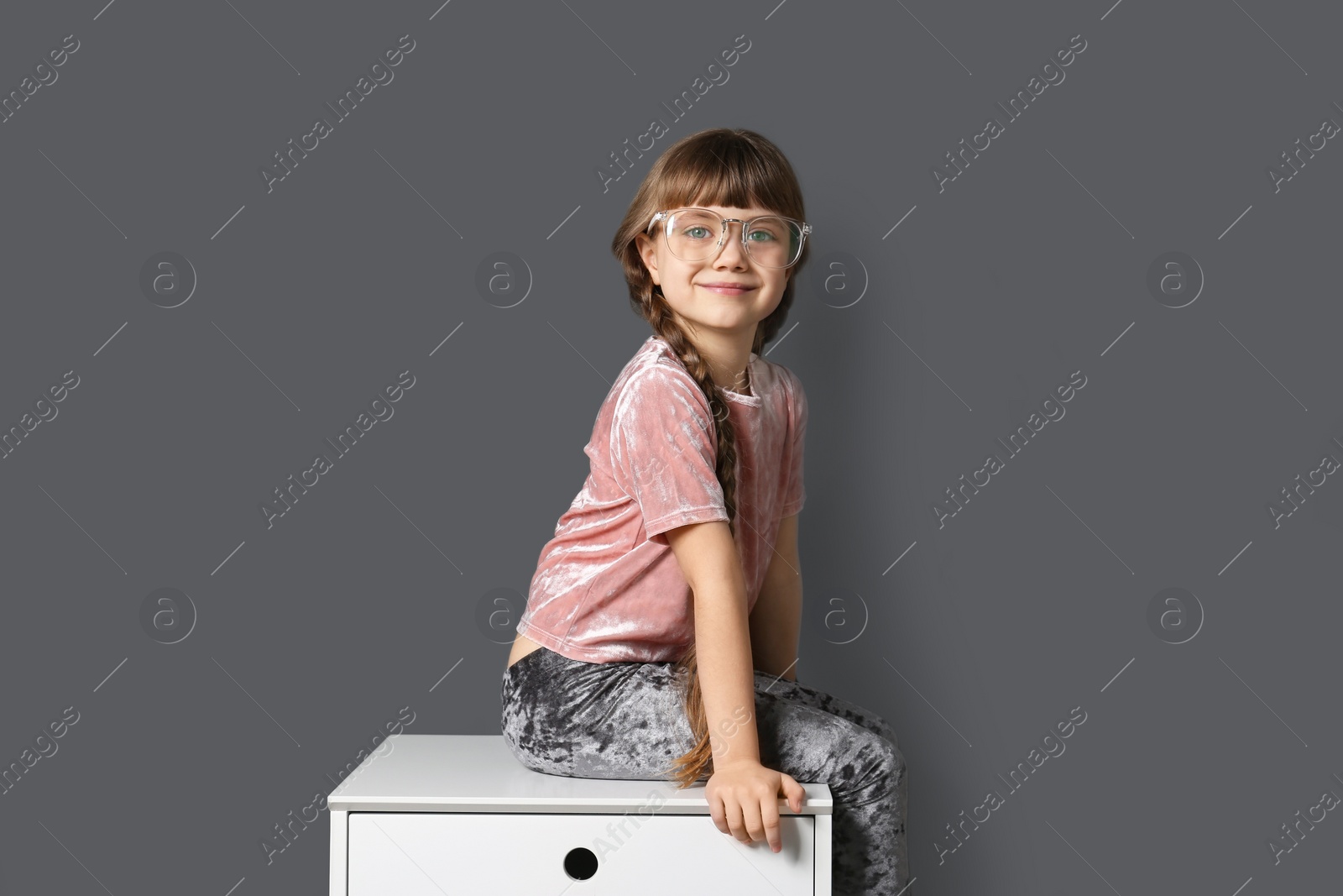 Photo of Cute little girl sitting on chest of drawers unit near gray wall