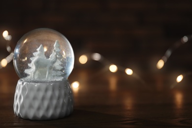 Photo of Snow globe with Christmas lights on wooden table. Space for text