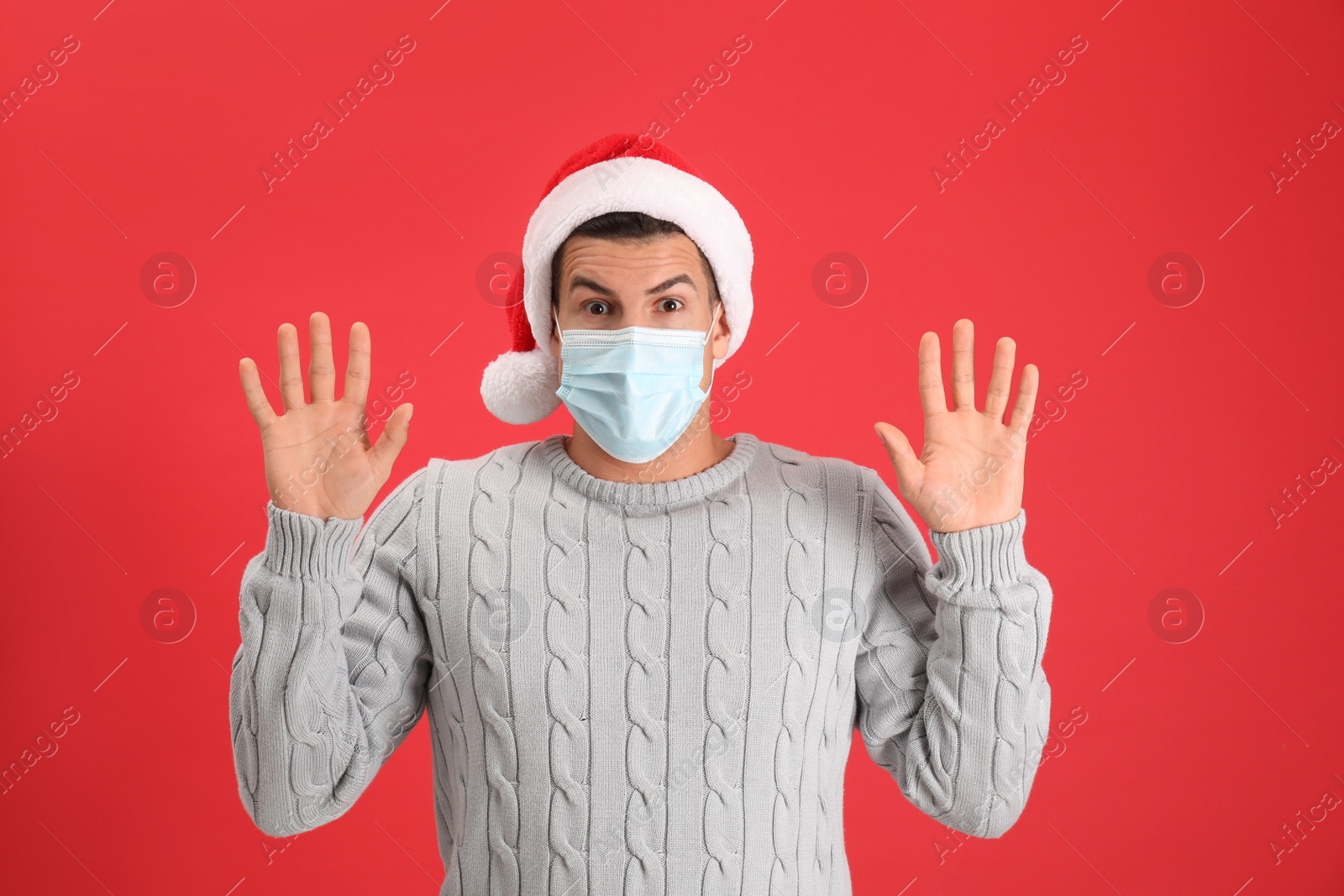Photo of Surprised man wearing Santa hat and medical mask on red background