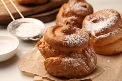 Photo of Delicious profiteroles with powdered sugar on parchment paper, closeup