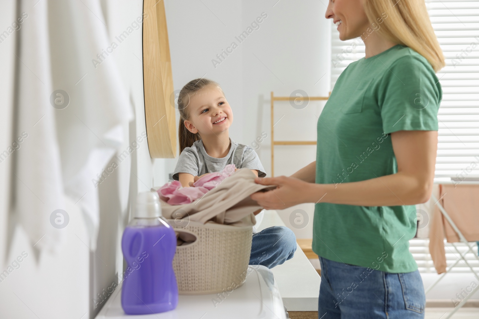 Photo of Mother and daughter taking out dirty clothes from basket in bathroom