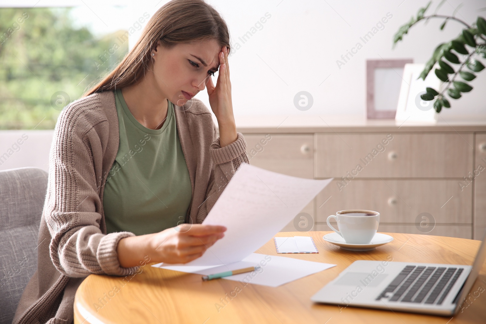 Photo of Worried woman reading letter at wooden table in room