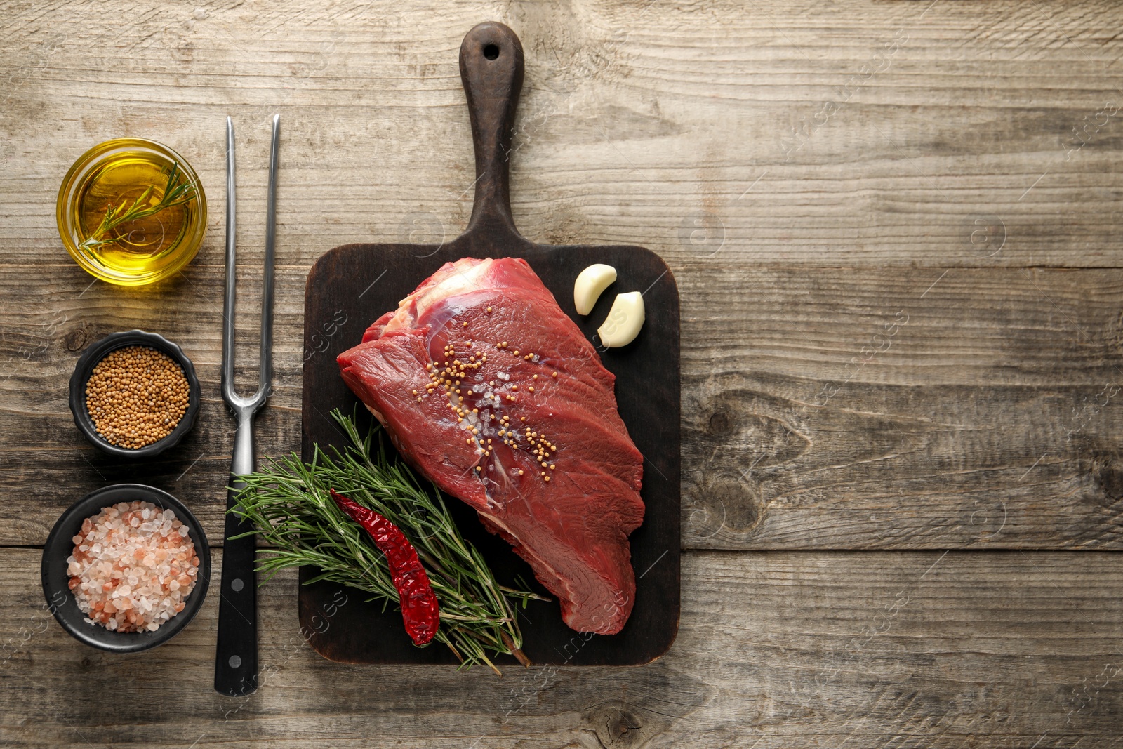 Photo of Piece of raw beef meat, rosemary, spices and fork on wooden table, flat lay. Space for text