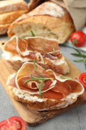 Tasty sandwiches with cured ham, tomatoes and rosemary on grey table, closeup