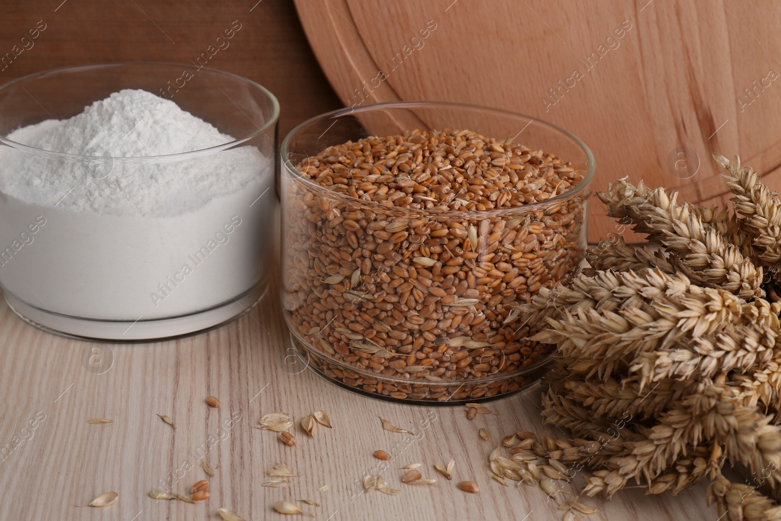 Photo of Wheat grains in bowl, spikes and flour on wooden table