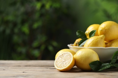 Photo of Fresh lemons and green leaves on wooden table. Space for text