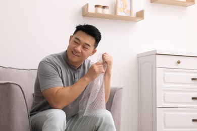 Photo of Happy asian man with bubble wrap indoors. Space for text