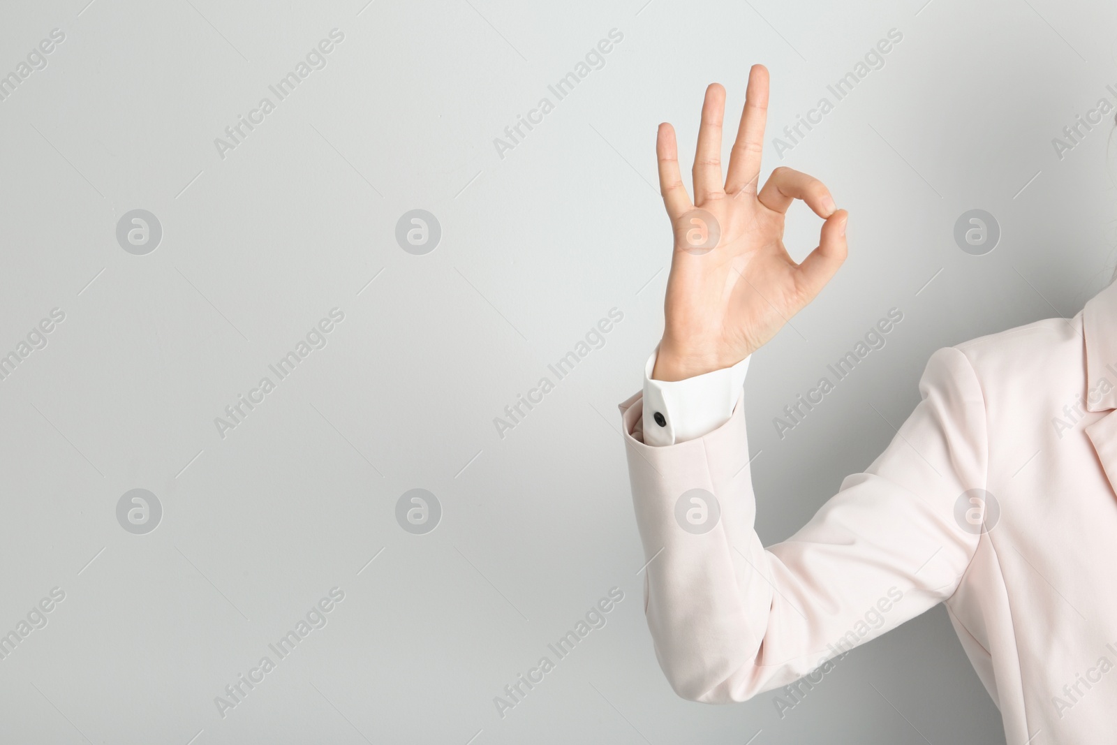 Photo of Young woman showing OK gesture on light background. Space for text