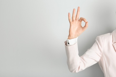 Young woman showing OK gesture on light background. Space for text