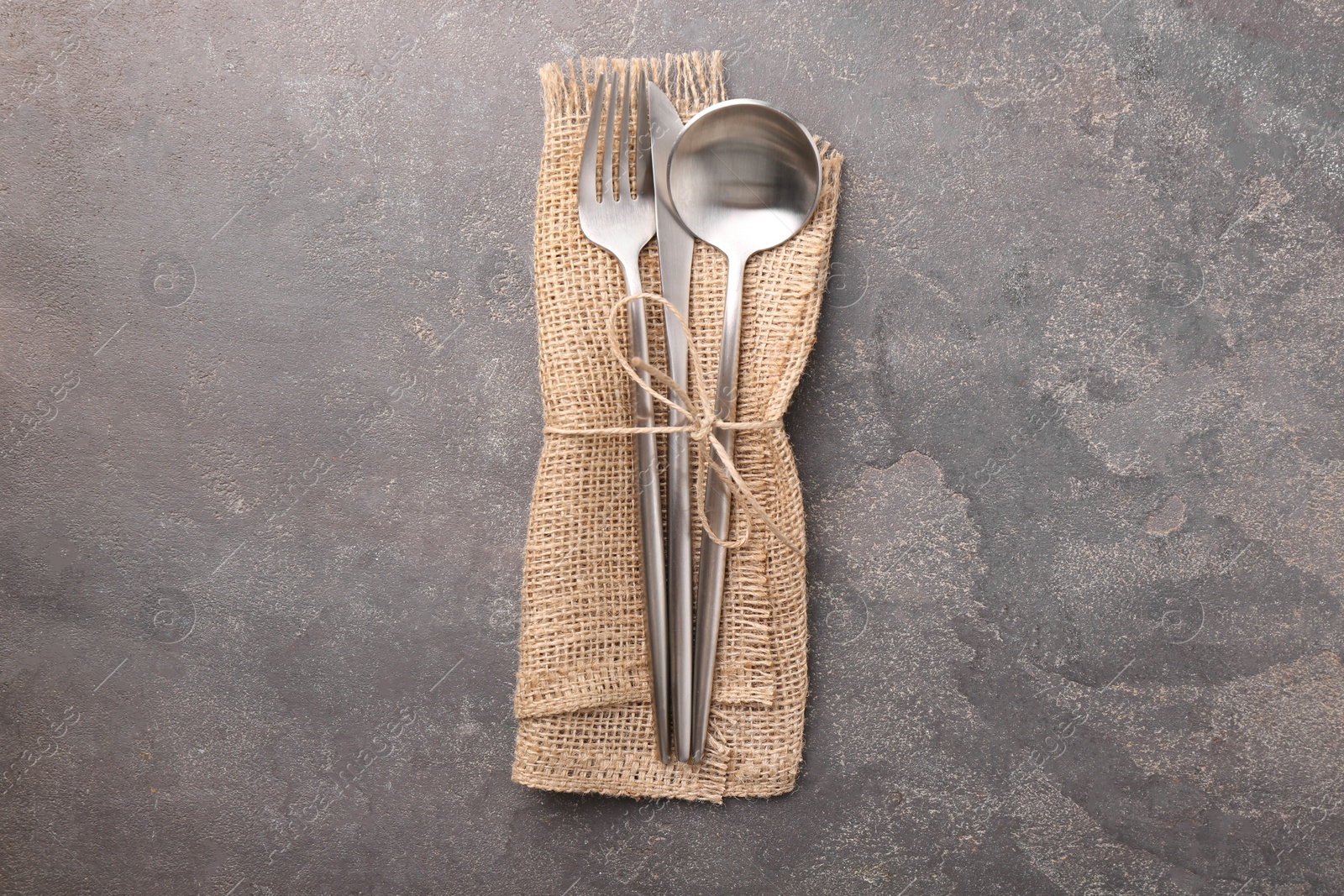 Photo of Set of stylish cutlery and napkin on grey textured table, top view