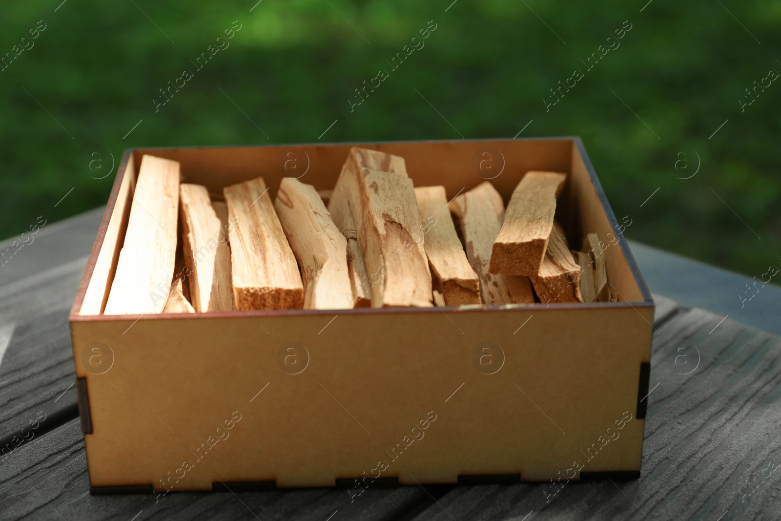 Photo of Box of many palo santo sticks on wooden table outdoors