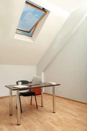 Stylish workplace with laptop and documents in attic room. Interior design