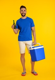 Photo of Happy man with cool box and bottle of beer on yellow background