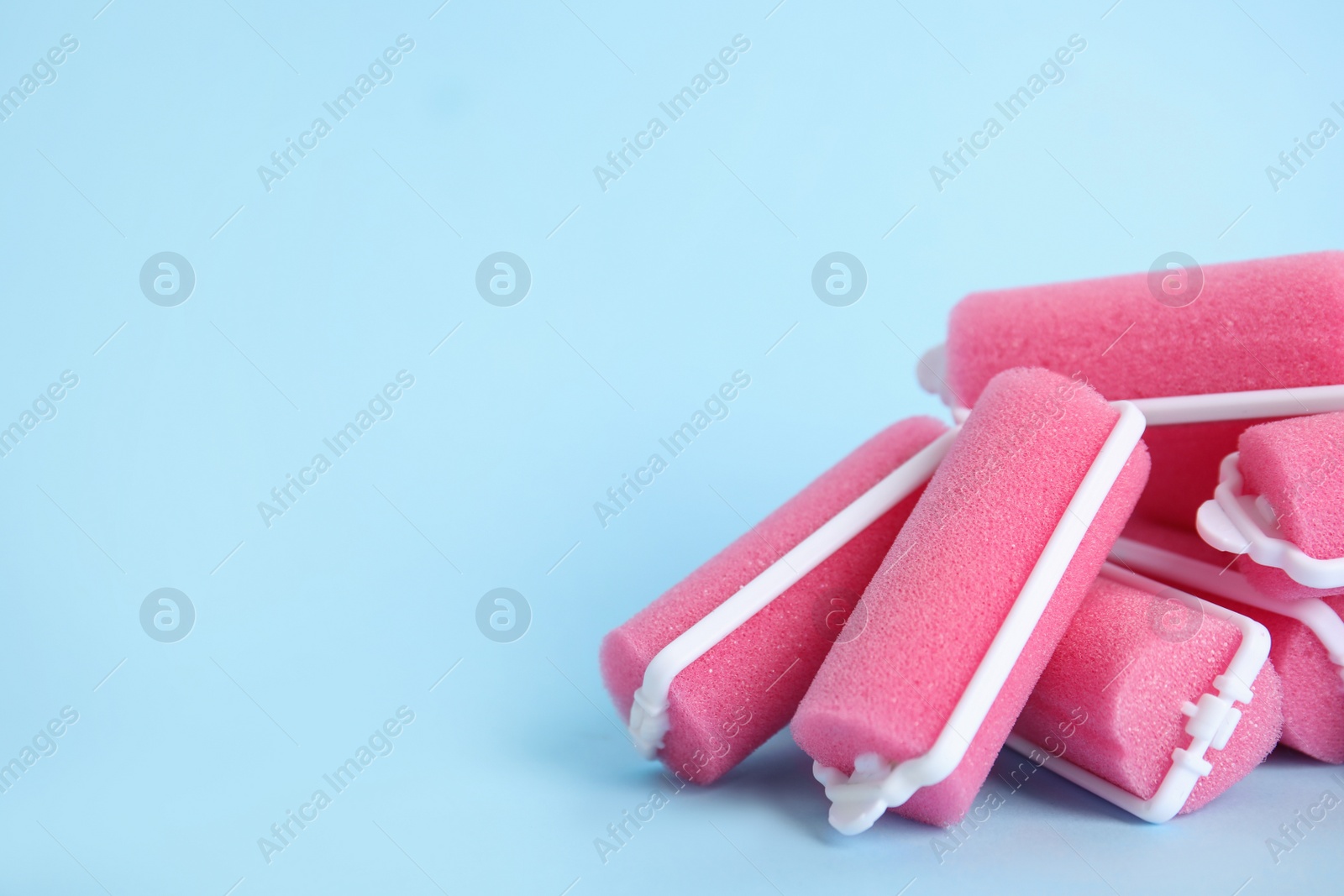 Photo of Many pink hair curlers on light blue background, space for text