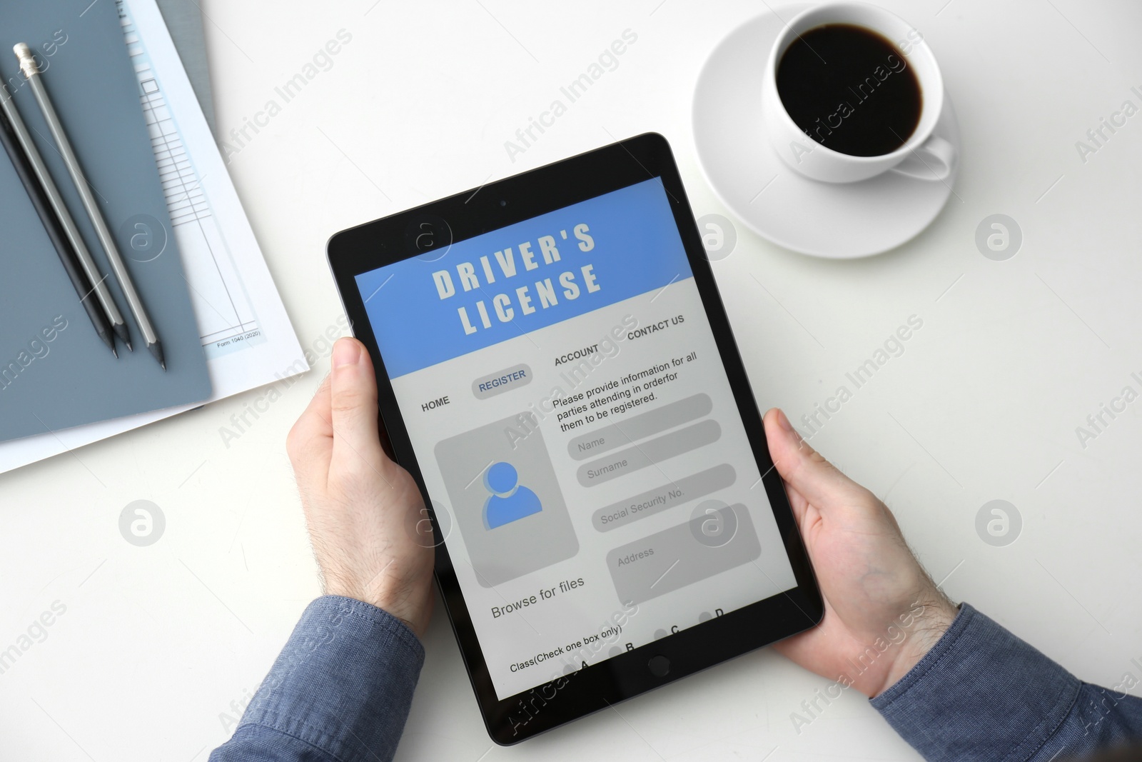 Photo of Man holding tablet with driver's license application form at white table, above view