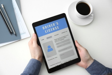 Man holding tablet with driver's license application form at white table, above view