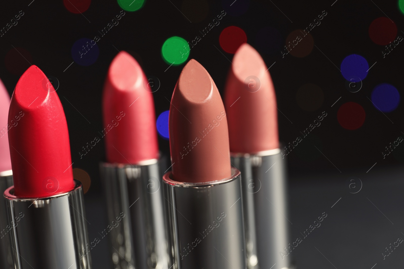 Photo of Different lipsticks against blurred lights. Cosmetic product