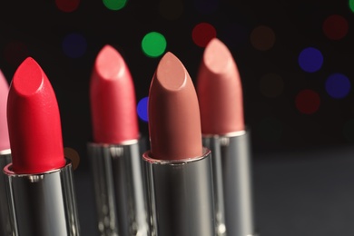 Photo of Different lipsticks against blurred lights. Cosmetic product