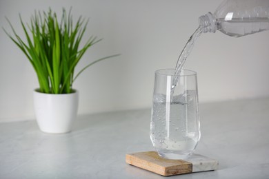 Pouring water from bottle into glass on white countertop in kitchen. Space for text