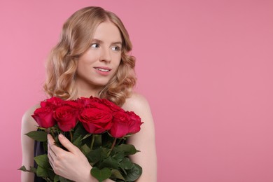 Photo of Beautiful woman with blonde hair holding bouquet of red roses on pink background. Space for text